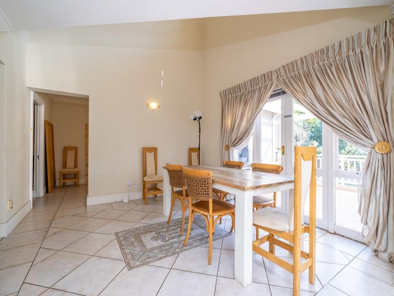 A bright dining area featuring tiled flooring, vaulted ceilings, and double glass doors providing access to an outdoor patio space.
