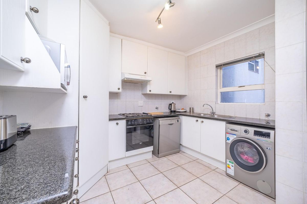 A functional kitchen featuring white cabinetry, granite countertops, a gas hob, built-in oven, and tiled flooring with integrated laundry appliance space.
