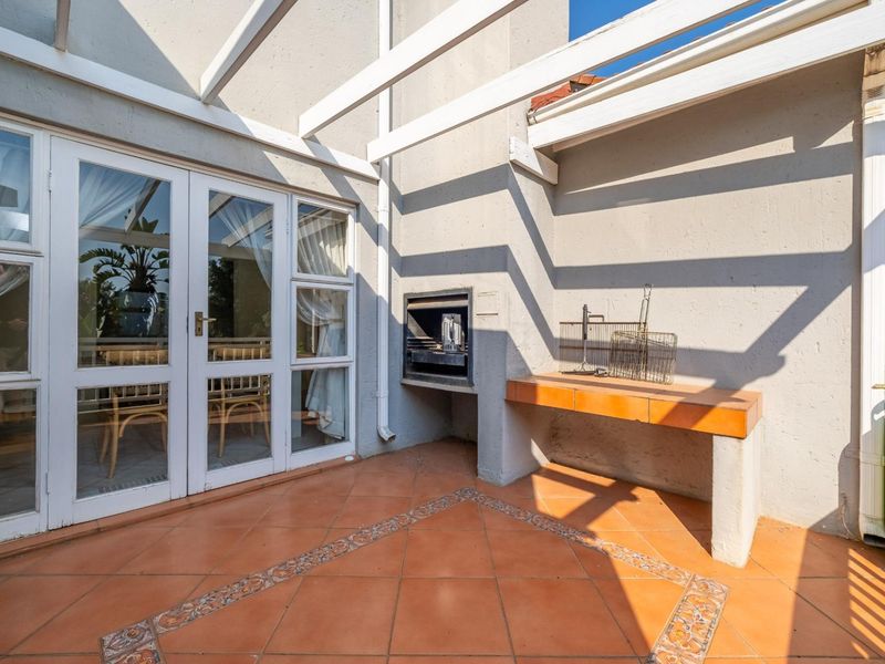 Covered patio area featuring a built-in braai, tiled flooring, and direct access to the interior through double glass doors.
