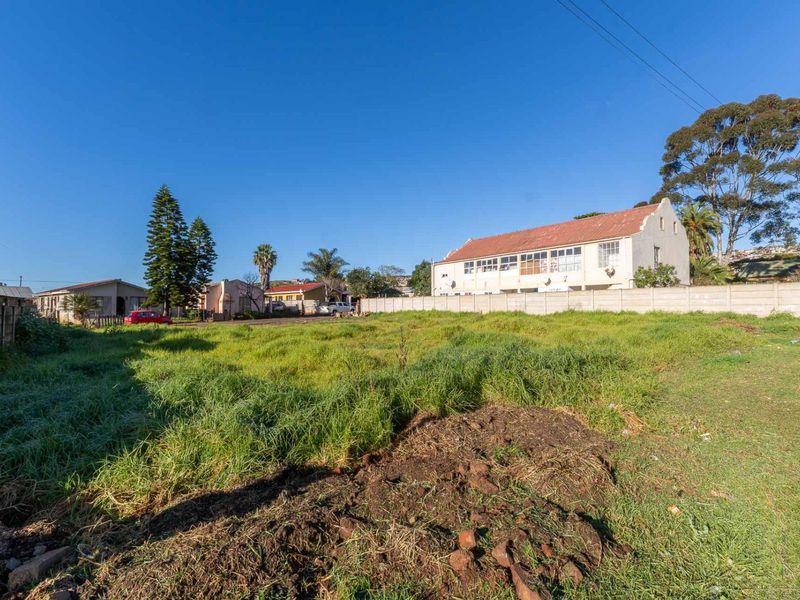 A vacant residential plot featuring overgrown grass and a precast concrete boundary wall in a suburban neighborhood setting.