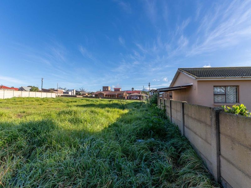 A view of a vacant residential plot featuring a precast concrete boundary wall and overgrown grass, situated in a suburban neighborhood.