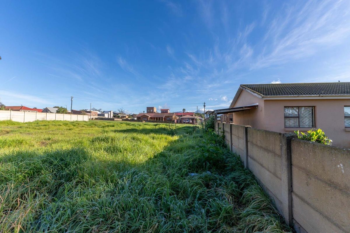 A view of a vacant residential plot featuring a precast concrete boundary wall and overgrown grass, situated in a suburban neighborhood.