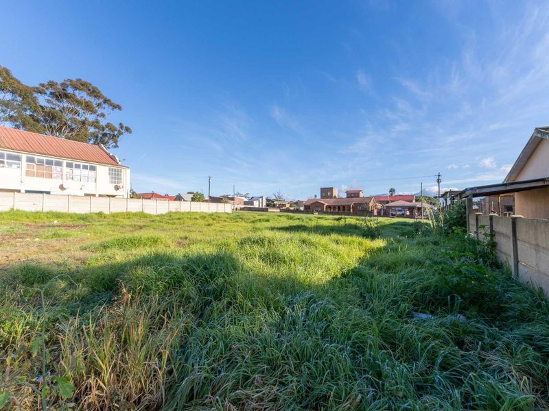 A vacant residential plot featuring overgrown grass and enclosed by precast concrete boundary walls, situated in a developed neighborhood.