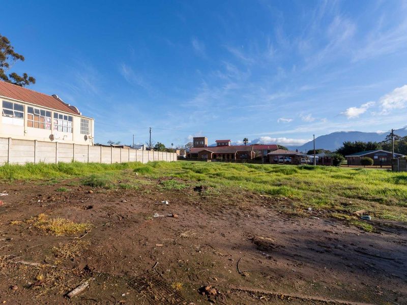 A vacant residential plot featuring a precast concrete boundary wall and open, unimproved land with mountain views in the background.