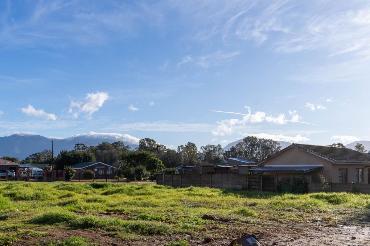 A vacant residential plot featuring a grassed surface and a precast concrete boundary wall, set against a scenic mountain backdrop.