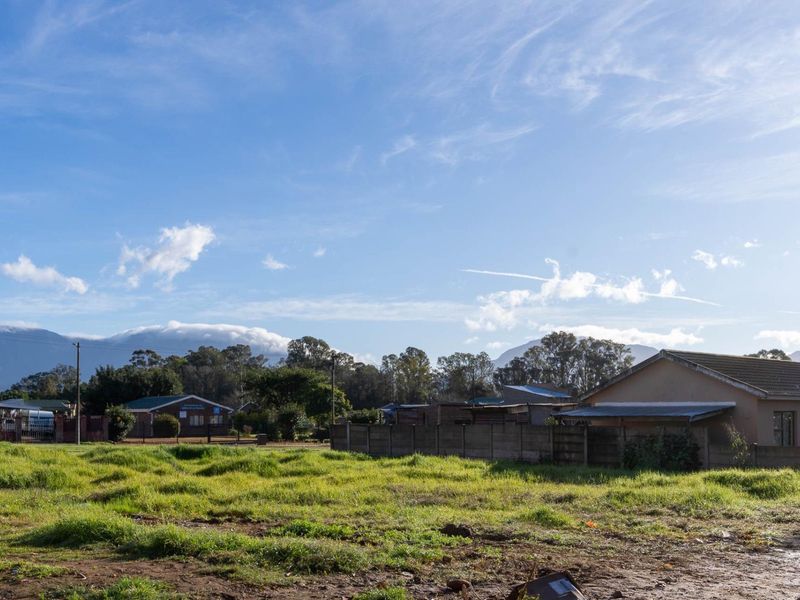 A vacant residential plot featuring a grassed surface and a precast concrete boundary wall, set against a scenic mountain backdrop.
