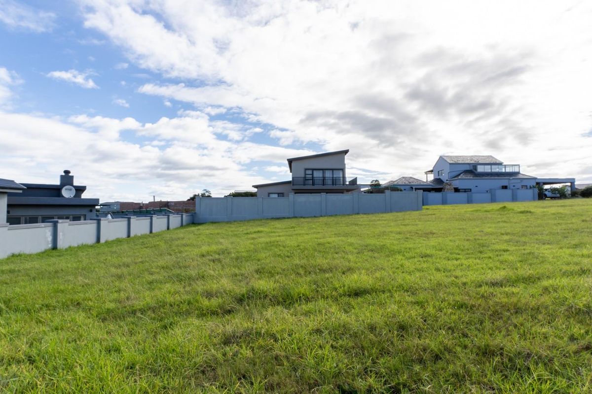 A vacant residential plot featuring a well-maintained grass lawn and a secure perimeter wall, situated in a developed neighborhood.
