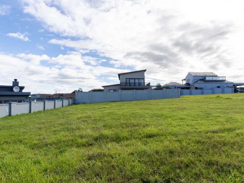 A vacant residential plot featuring a well-maintained grass lawn and a secure perimeter wall, situated in a developed neighborhood.