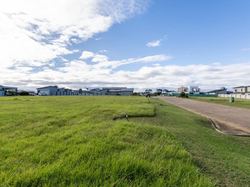 A vacant residential plot of land featuring a grassed surface adjacent to a paved street in a developed neighborhood.