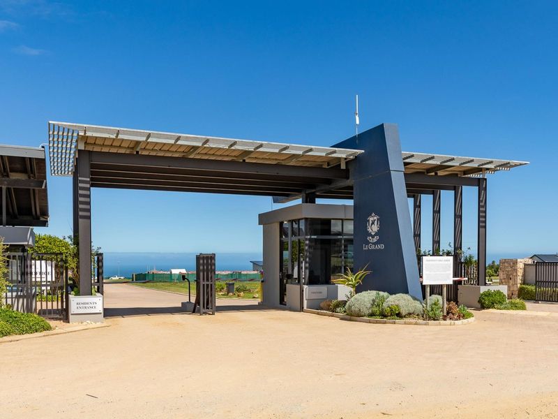 Modern gated entrance and security gatehouse for Le Grand estate, featuring a steel structure with integrated solar panels and landscaped surroundings.