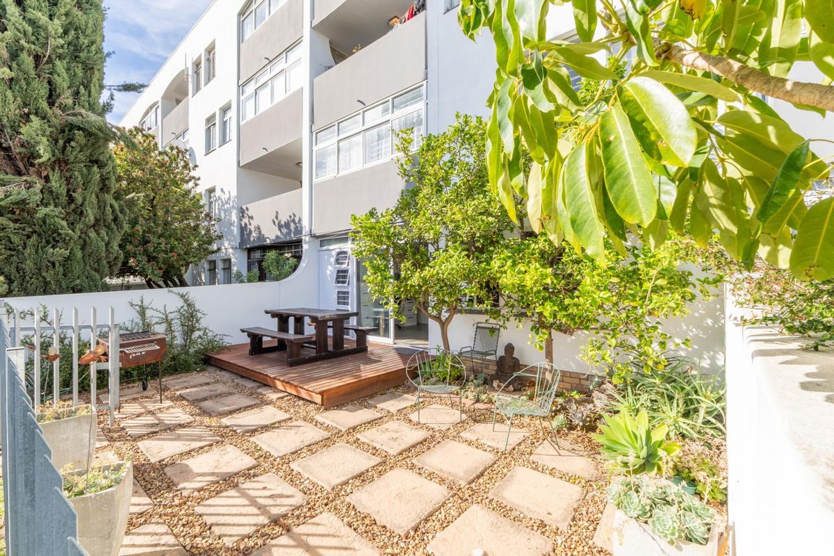 A private rear courtyard featuring a timber deck, paved patio area, and established garden greenery, providing direct access to the apartment.