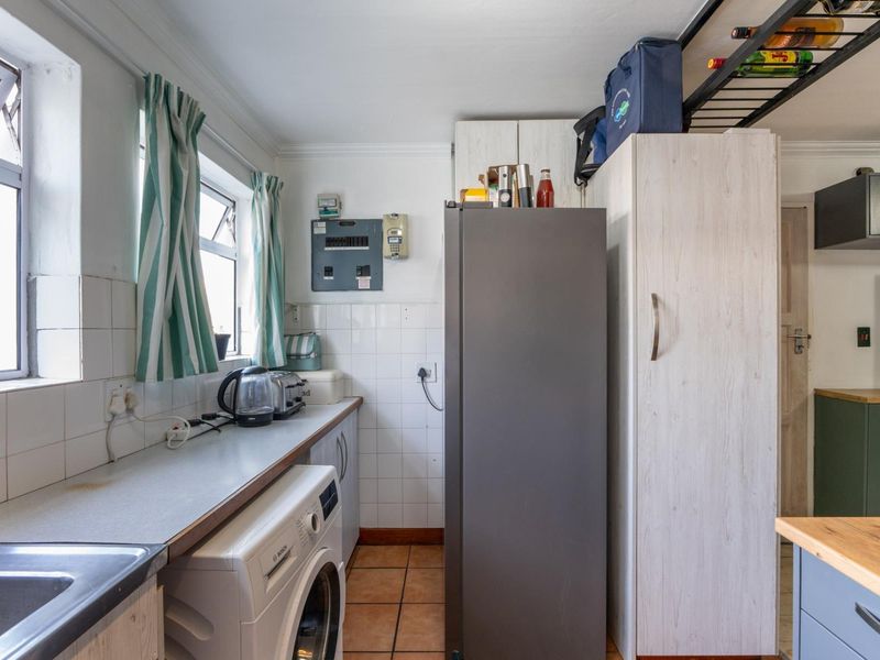 A functional scullery area featuring built-in cabinetry, tiled splashbacks, a stainless steel sink, and dedicated space for laundry appliances.