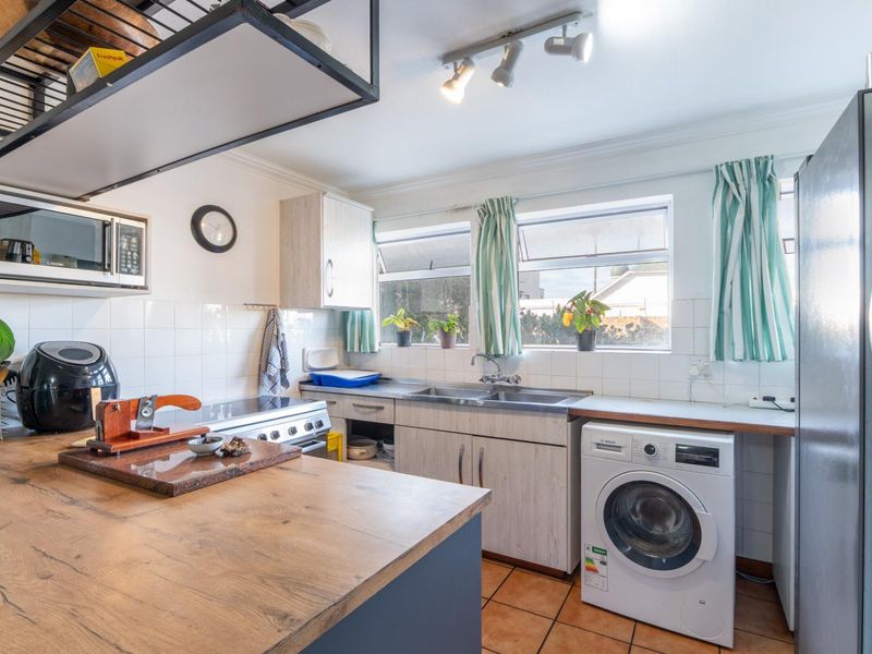 A functional kitchen featuring wood-look cabinetry, tiled backsplash, stainless steel sink, built-in oven, and integrated laundry appliance space with tiled flooring.