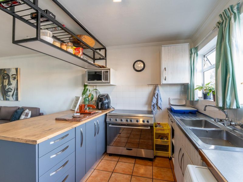 A functional kitchen featuring blue cabinetry, wooden countertops, a stainless steel stove, and overhead metal shelving with a tiled backsplash and double sink.