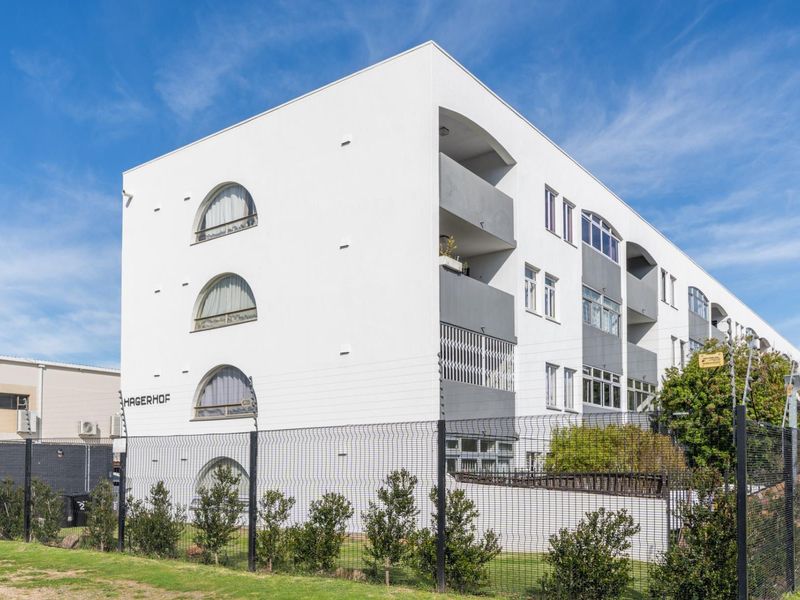 Exterior view of the Hagerhof apartment building featuring a modern white facade, arched windows, and secure perimeter fencing.