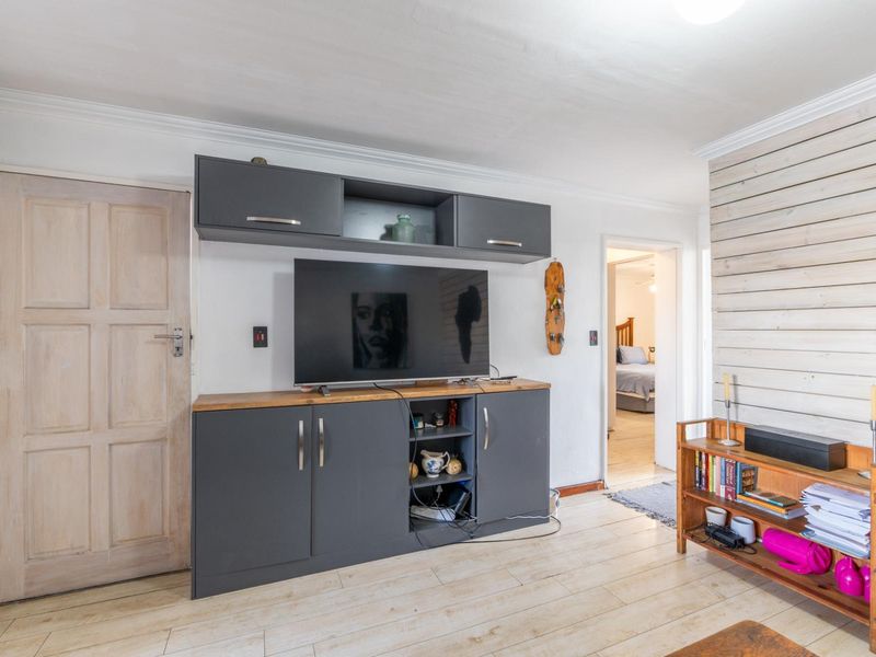 Living room featuring built-in grey cabinetry, timber wall paneling, and light-toned laminate flooring, providing a functional space with direct access to adjacent rooms.