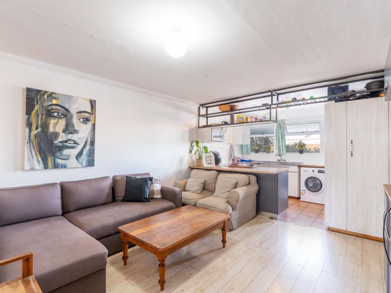 Open plan living area featuring laminate flooring and a compact kitchen space with built-in cabinetry and shelving.