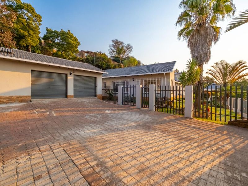 Front view of the property featuring a paved driveway, double garage, and secure metal fencing with established garden surroundings.