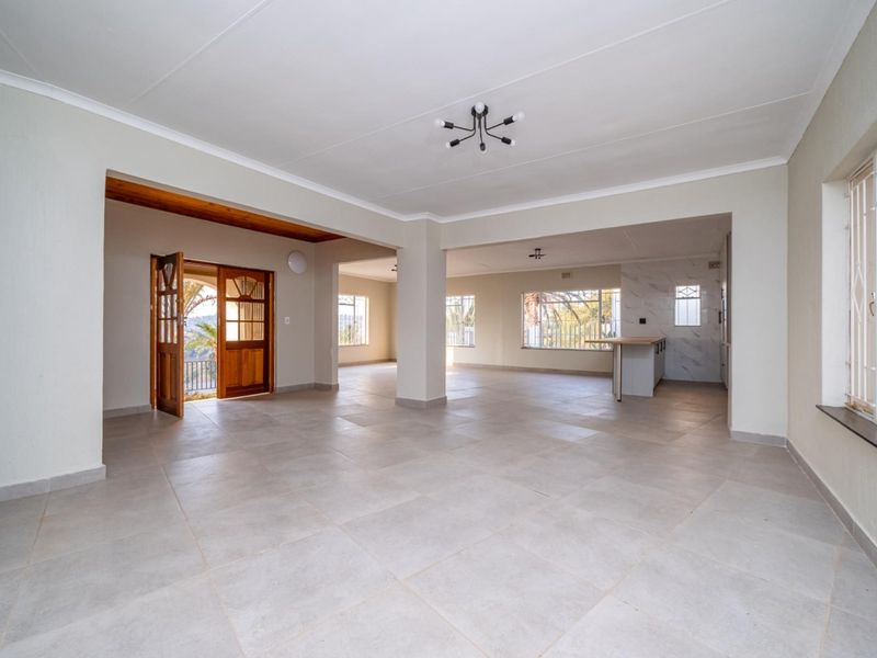 Spacious open-plan living area featuring neutral tiled flooring, clean finishes, and direct access to an outdoor space through a timber door.