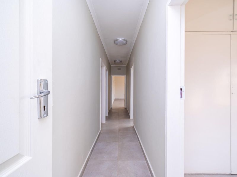 A clean, well-lit hallway featuring neutral tiled flooring and built-in storage cupboards, providing a bright and functional transition space within the home.