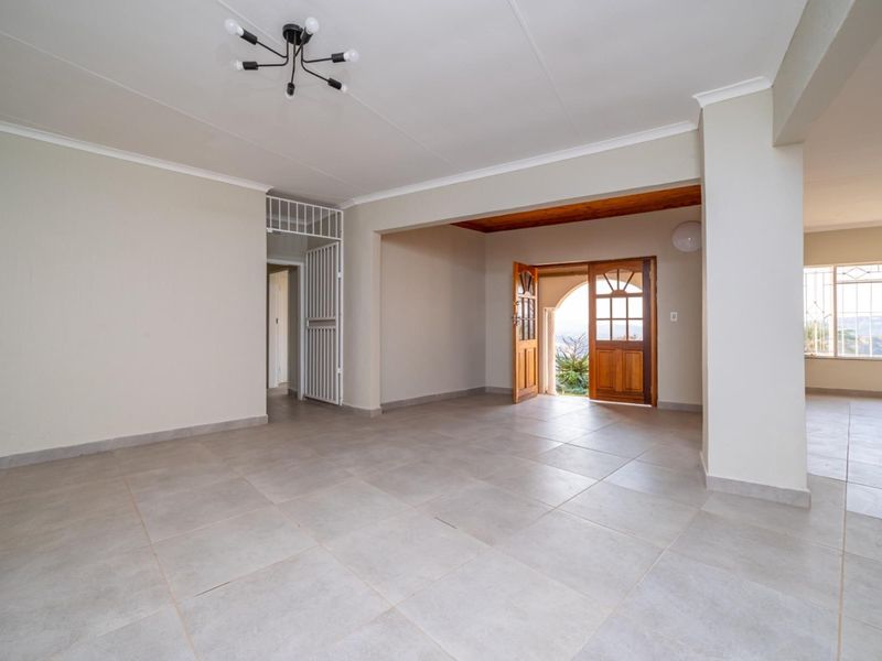 A spacious, open-plan living area featuring neutral tiled flooring, modern lighting, and wooden double doors leading to an outdoor space.