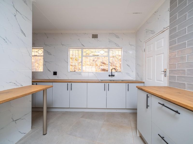 A clean, empty kitchen featuring marble-look wall tiles, wooden countertops, and modern cabinetry, offering a functional space ready for personalization.