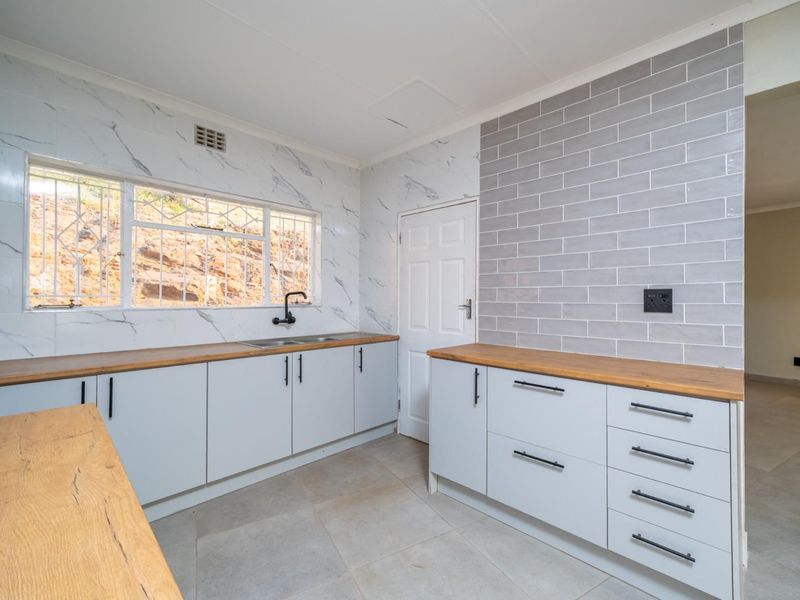 Modern kitchen featuring light grey cabinetry, warm wooden countertops, subway tile splashback, and marble-effect wall tiles with a double sink and black fixtures.