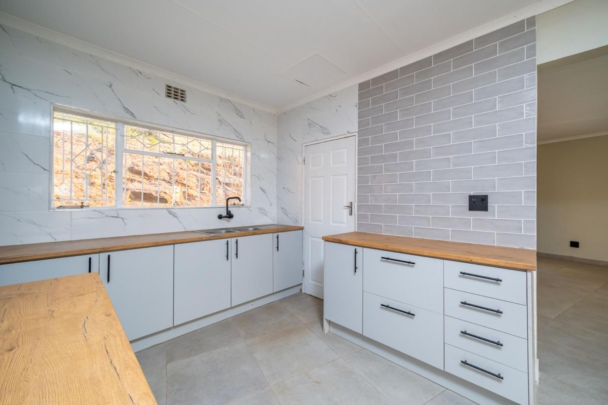 Modern kitchen featuring light grey cabinetry, warm wooden countertops, subway tile splashback, and marble-effect wall tiles with a double sink and black fixtures.