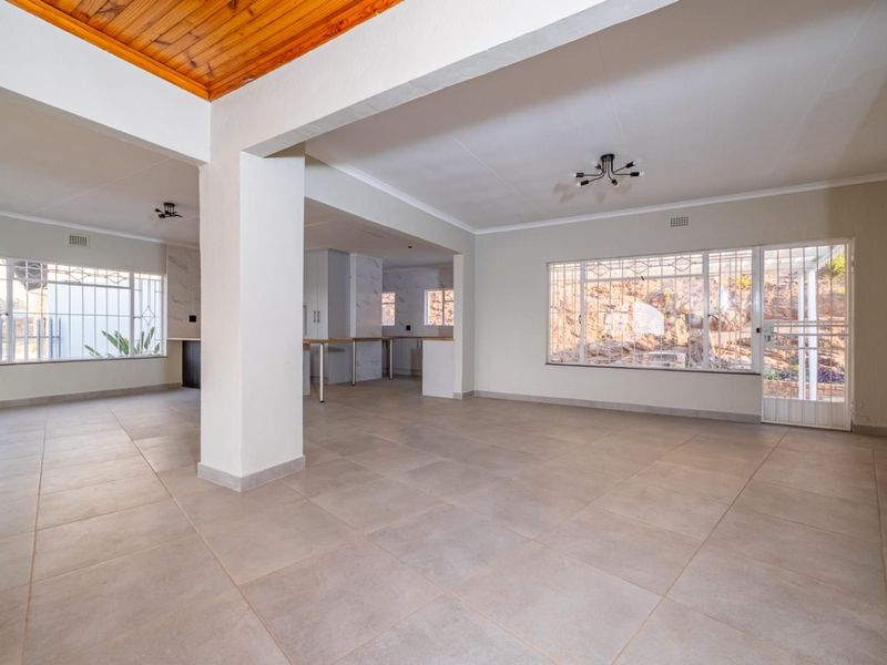 Spacious open-plan living and kitchen area featuring neutral tiled flooring, exposed timber ceiling details, and large windows with security bars.