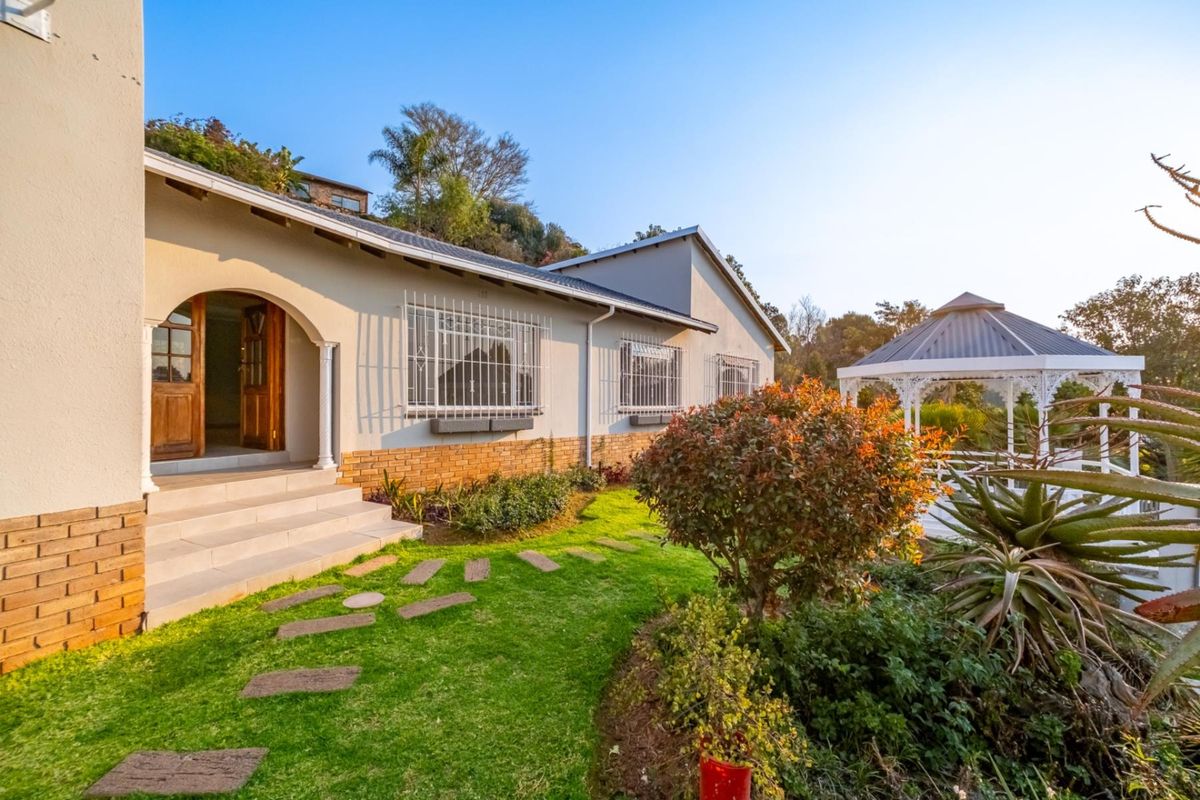 A well-maintained rear exterior view featuring a landscaped garden, a charming gazebo, and an arched entrance with stepped access to the home.
