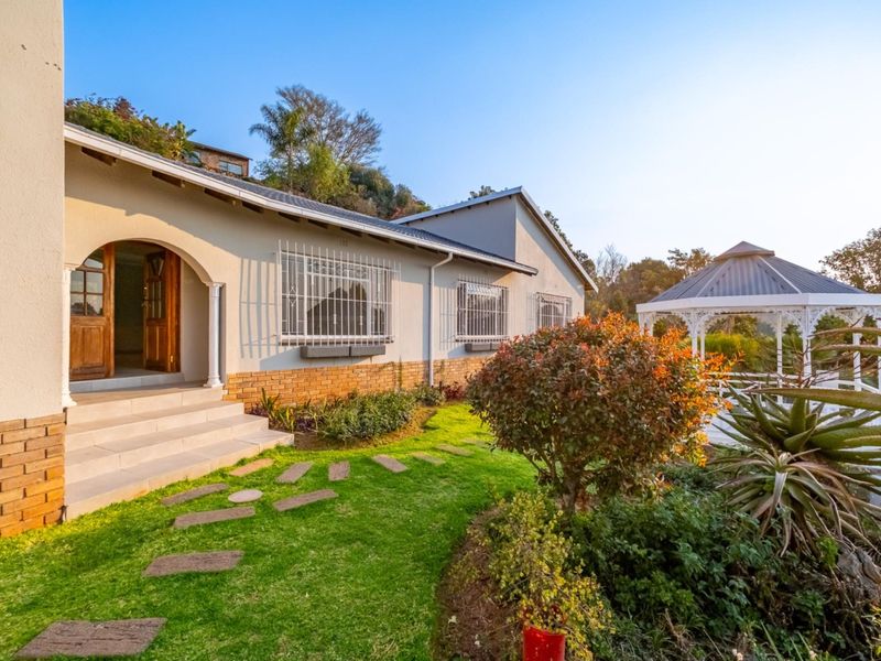 A well-maintained rear exterior view featuring a landscaped garden, a charming gazebo, and an arched entrance with stepped access to the home.