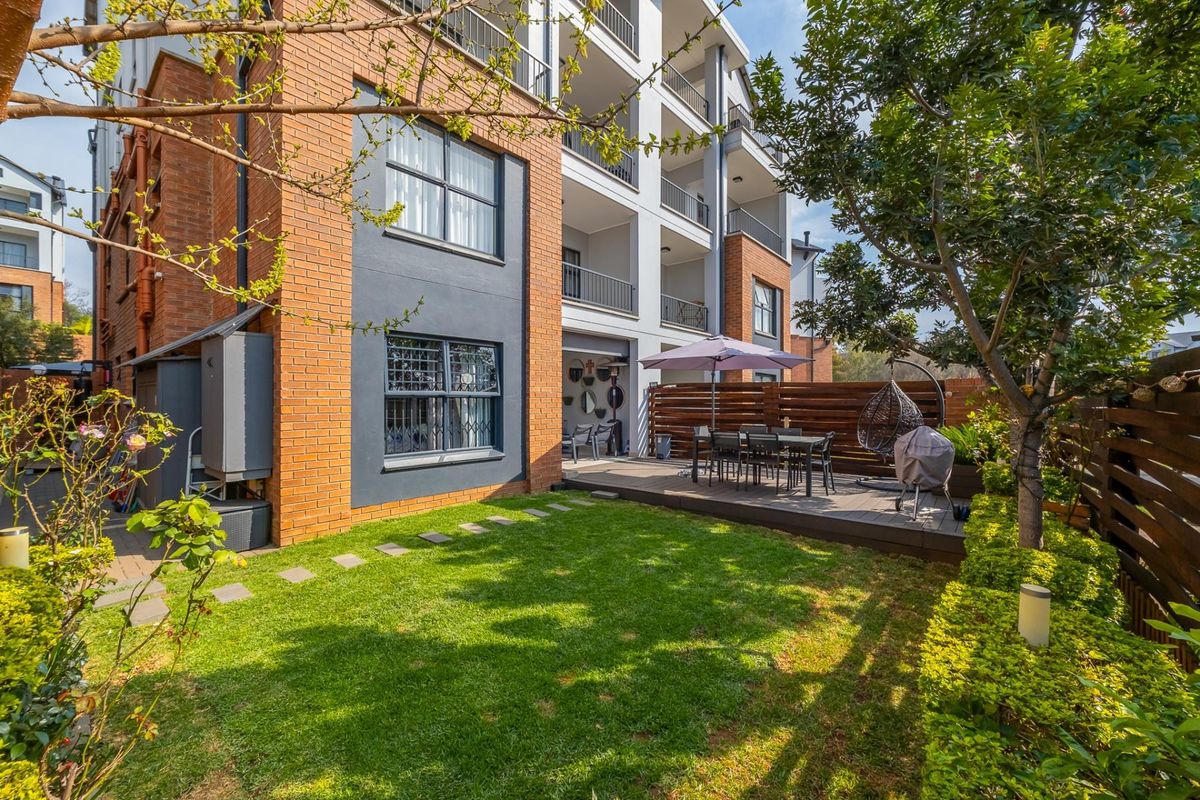 Rear view of the apartment building featuring a private garden, timber decking, and access to upper-level balconies.