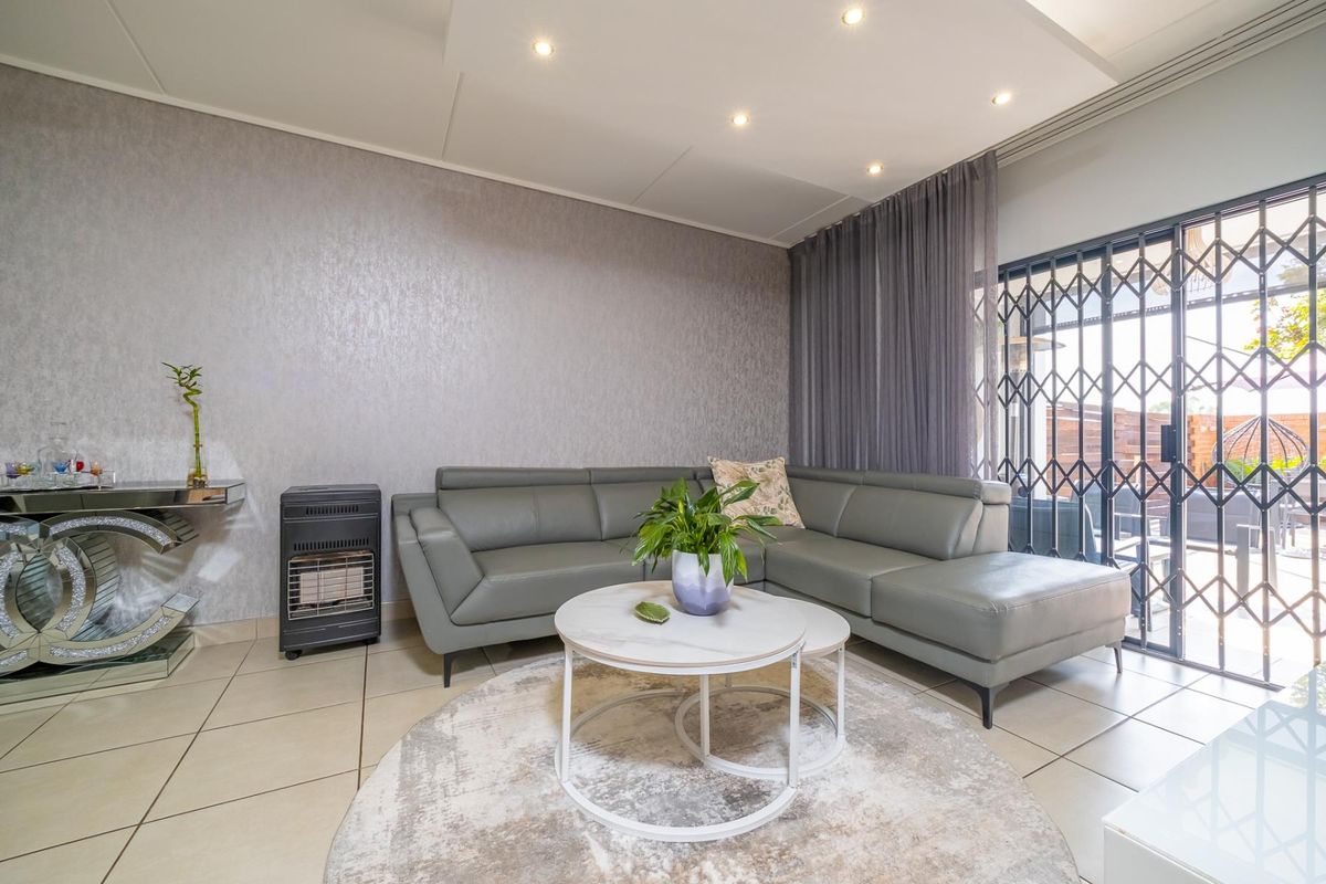 A well-maintained living room featuring tiled flooring, recessed ceiling lights, and a sliding glass door with a security gate leading to the patio.