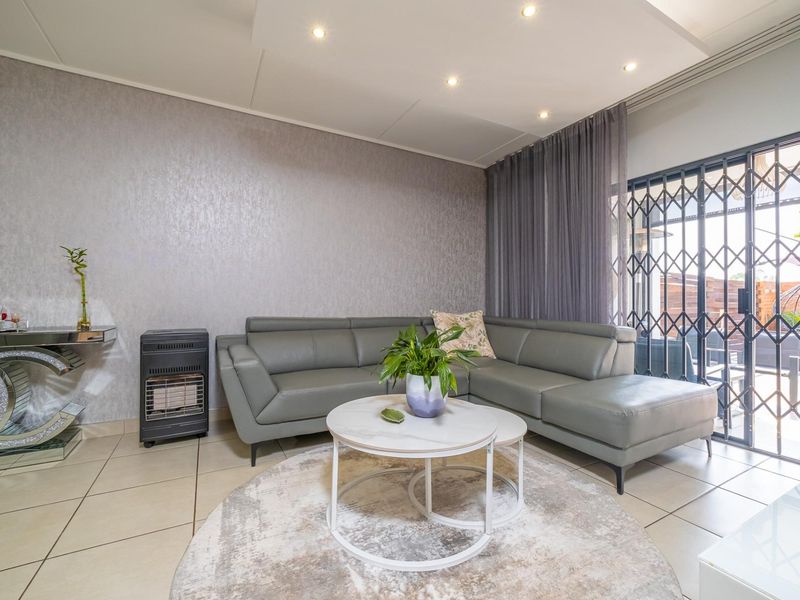 A well-maintained living room featuring tiled flooring, recessed ceiling lights, and a sliding glass door with a security gate leading to the patio.