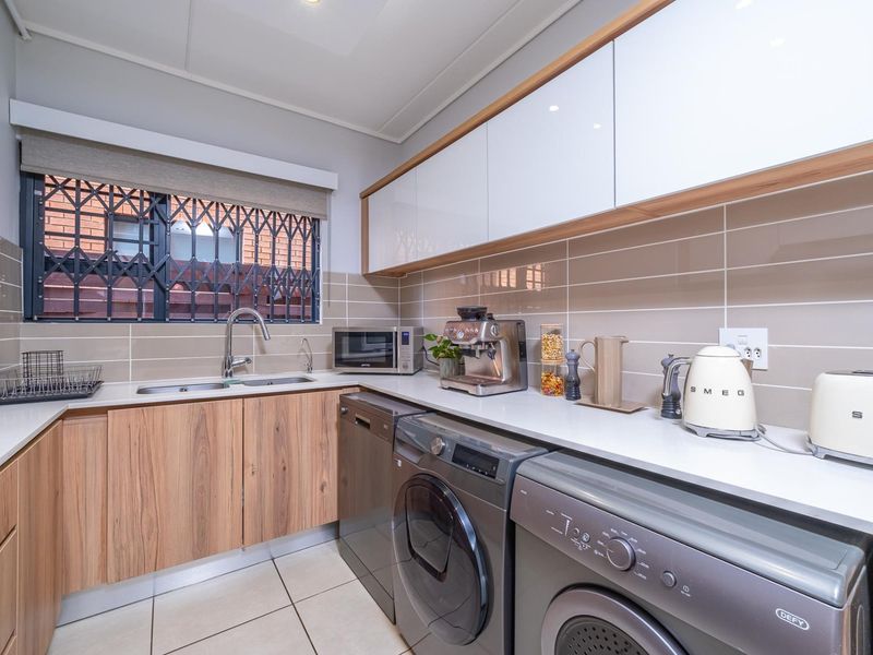 Modern kitchen featuring wood-grain cabinetry, stone countertops, tiled backsplash, and integrated space for laundry appliances.