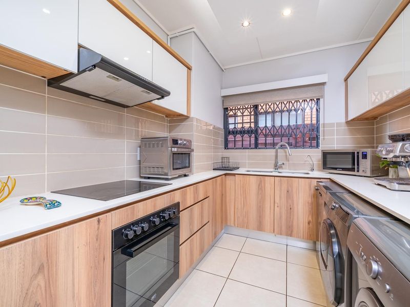 Modern kitchen featuring wood-finish cabinetry, white countertops, integrated appliances, tiled backsplash, and a functional layout with ample storage and workspace.