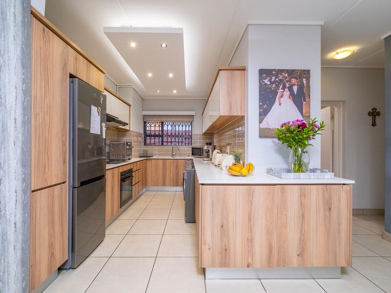 Modern kitchen featuring light wood-grain cabinetry, stone-look countertops, integrated appliances, and recessed ceiling lighting with a clean, functional layout.