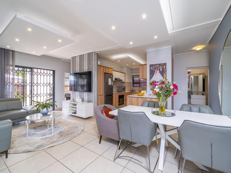 Modern open-plan living and dining area featuring tiled floors, recessed ceiling lighting, and a well-appointed kitchen with built-in cabinetry and appliances.