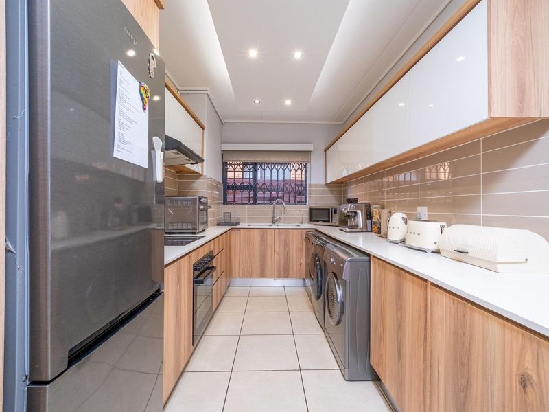 Modern galley-style kitchen featuring wood-grain cabinetry, white stone countertops, tiled backsplash, integrated appliances, and recessed ceiling lighting.