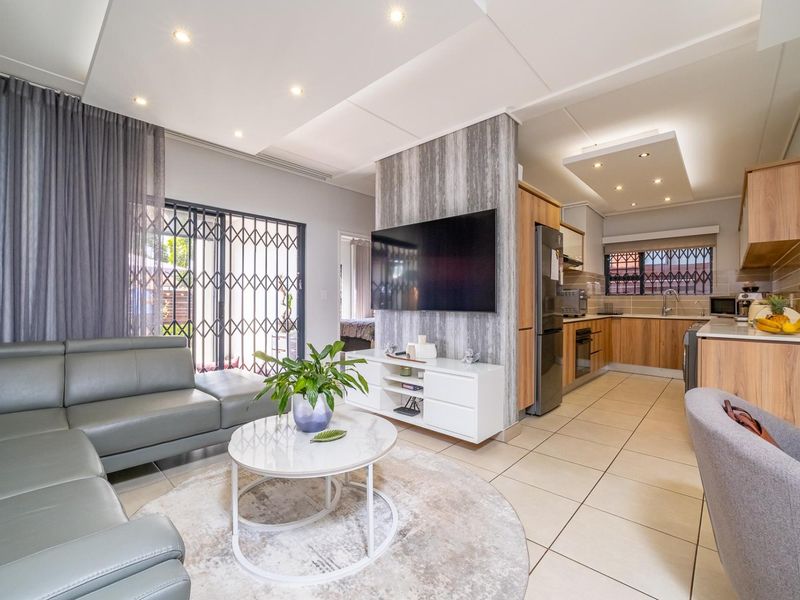 Modern open-plan living area featuring a well-appointed kitchen with wood-finish cabinetry, tiled floors, and recessed lighting, seamlessly flowing into the lounge space.