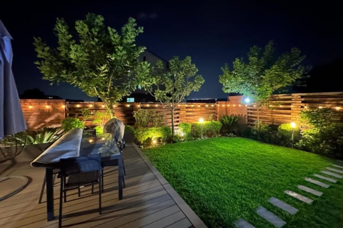 A beautifully landscaped rear garden featuring timber decking, a manicured lawn, stone pathways, and ambient integrated lighting, creating an inviting outdoor entertainment space.
