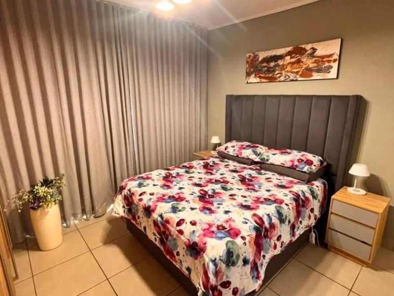A well-maintained bedroom featuring neutral tiled flooring, a modern ceiling light fixture, and full-length curtain tracks.