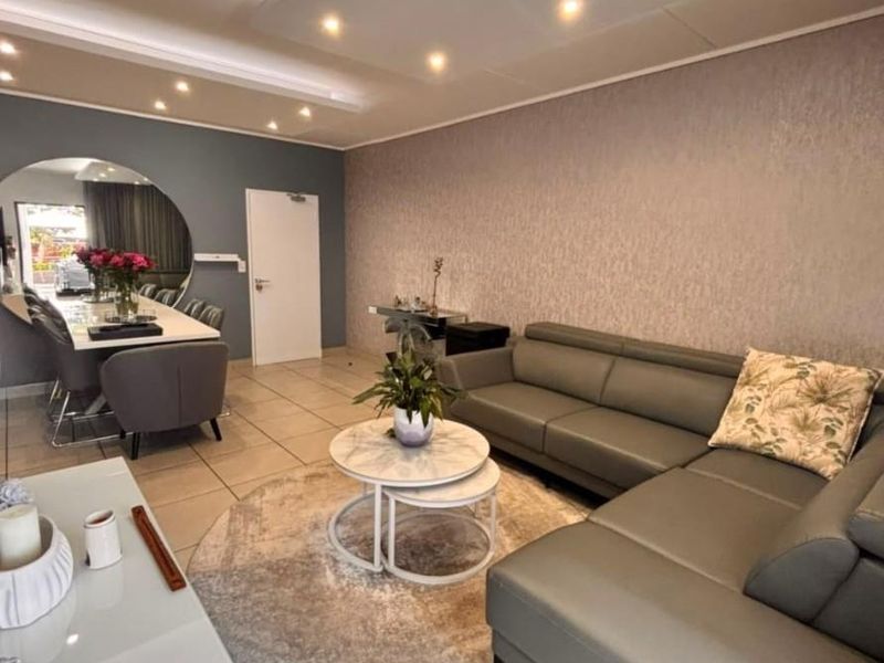 Spacious open-plan living and dining area featuring modern recessed ceiling lighting, neutral tiled flooring, and a stylish textured feature wall.
