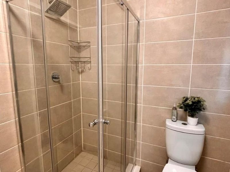 A clean bathroom featuring a glass-enclosed shower and a standard toilet with neutral wall and floor tiling.
