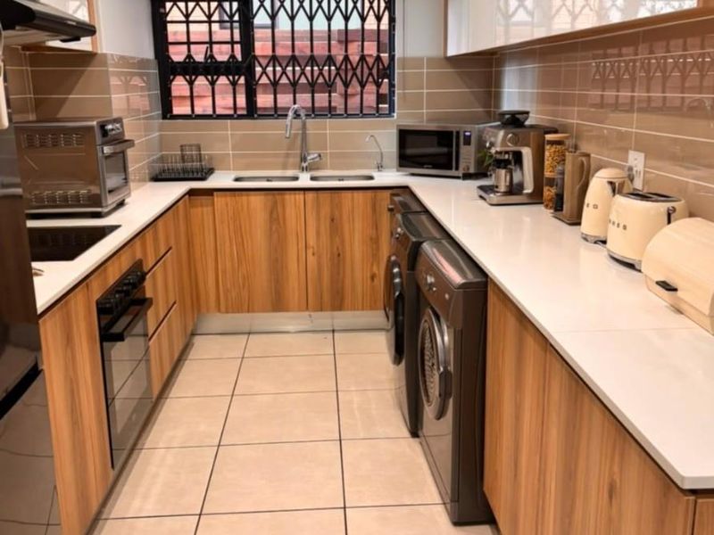 Modern galley-style kitchen featuring wood-finish cabinetry, white stone countertops, integrated appliances, tiled backsplash, and recessed lighting.