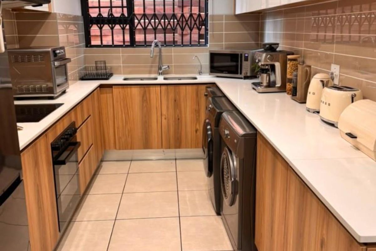 Modern galley-style kitchen featuring wood-finish cabinetry, white stone countertops, integrated appliances, tiled backsplash, and recessed lighting.