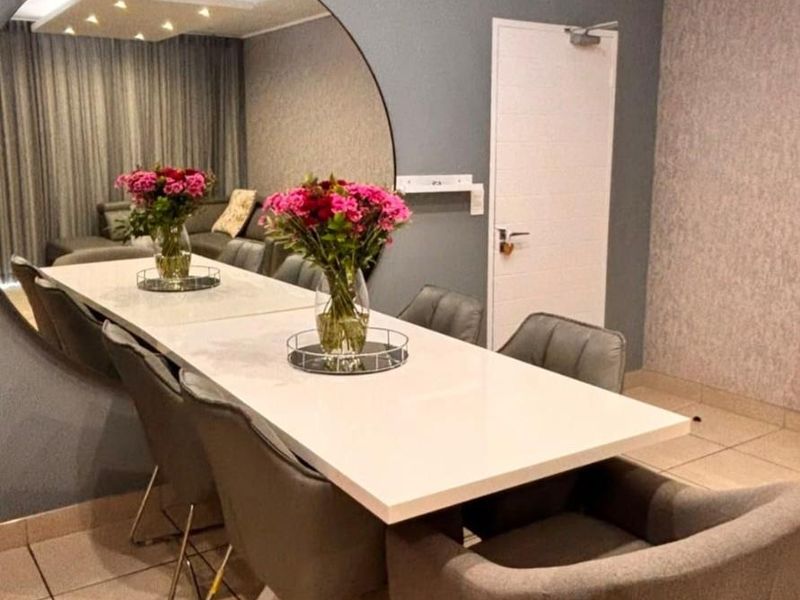 A modern dining area featuring tiled flooring, textured accent wallpaper, recessed ceiling lighting, and a large circular wall mirror.