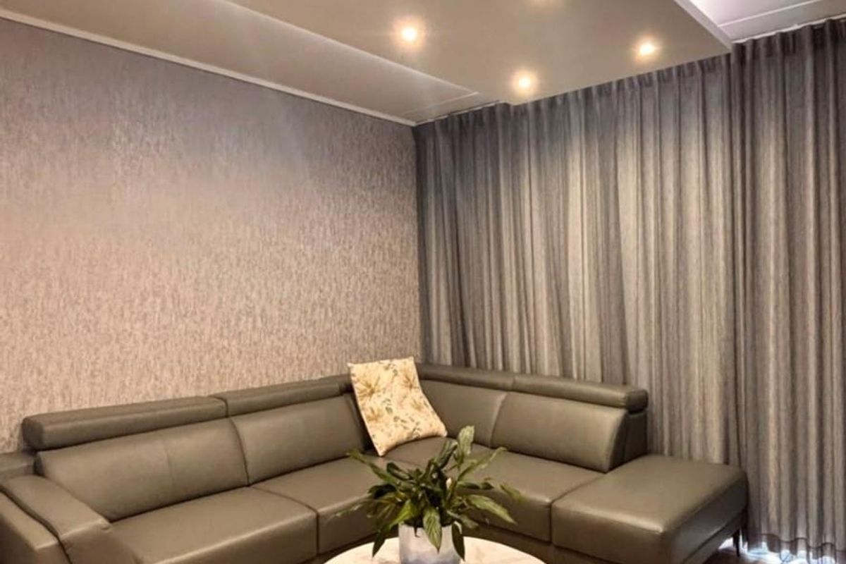 A well-maintained living room featuring a modern recessed ceiling with integrated downlights, textured wallpaper, and neutral tiled flooring.