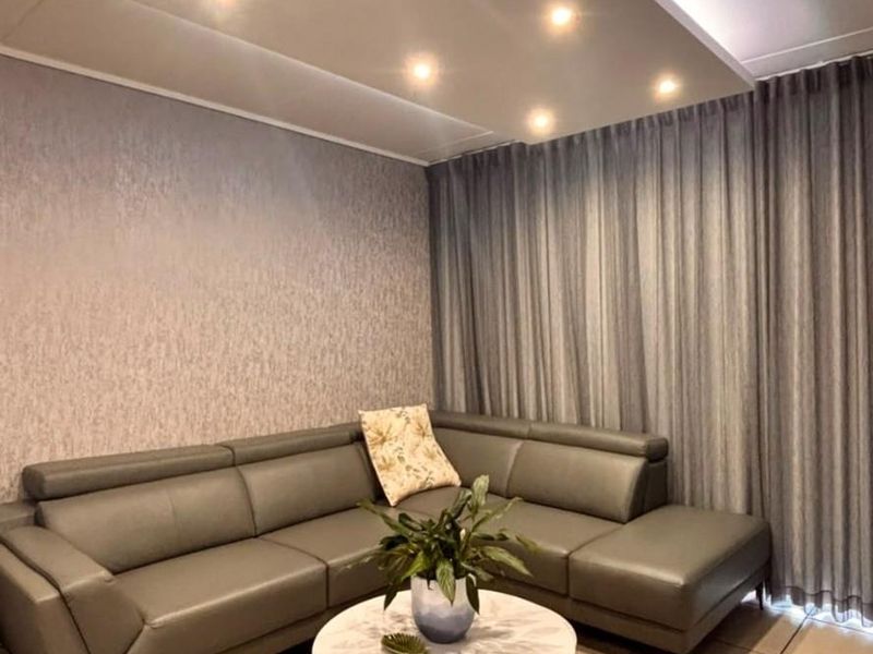 A well-maintained living room featuring a modern recessed ceiling with integrated downlights, textured wallpaper, and neutral tiled flooring.