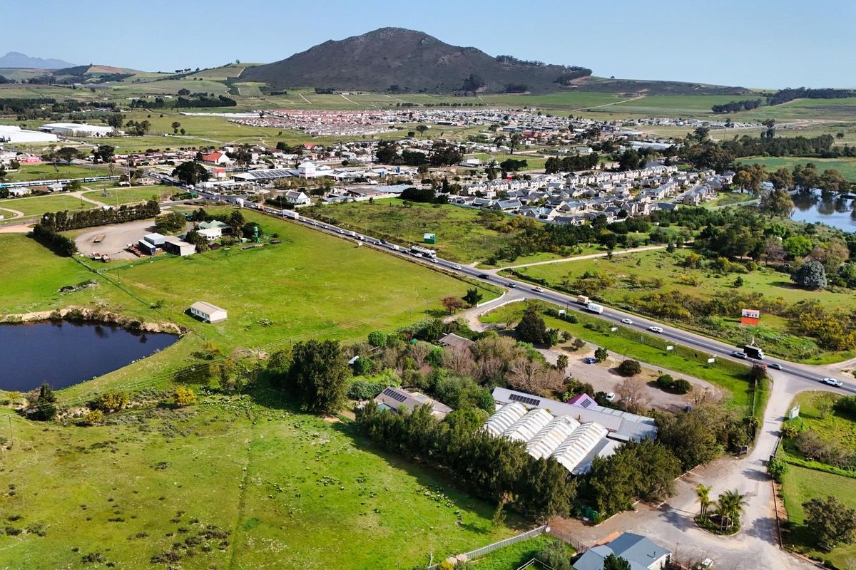 Aerial view of the commercial property featuring a greenhouse structure, solar panels, and surrounding land with a dam and road access.